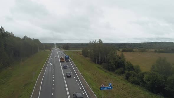 The Drone Flies Along a Busy Highway Behind Cars Trucks and Cars Move in the Stream Along a Fourlane