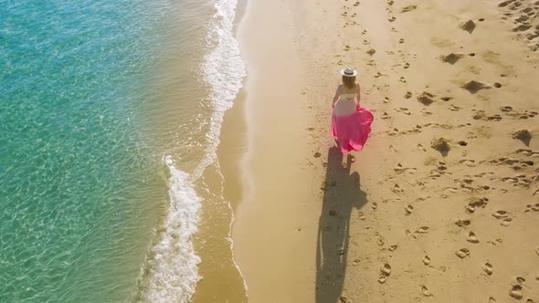 Happy Woman in Pink Beach Dress Walking By Scenic Tropical Ocean Beach at Sunset alt