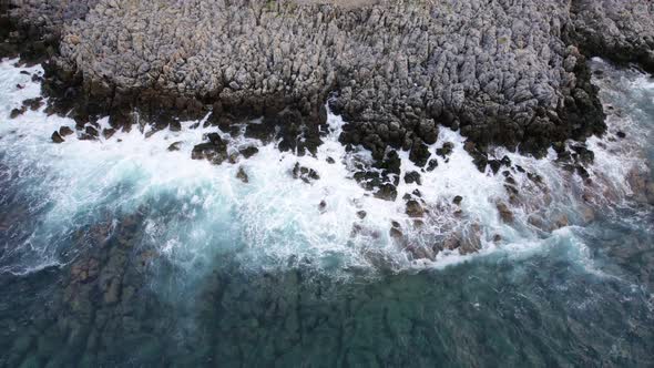 Aerial top view 4k footage by drone of ocean blue waves break on the high cliff of a rocky mountain alt