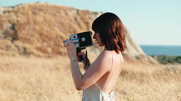 Beautiful Girl Makes Shots with Vintage Camera in Yellow Countryside in Summer alt