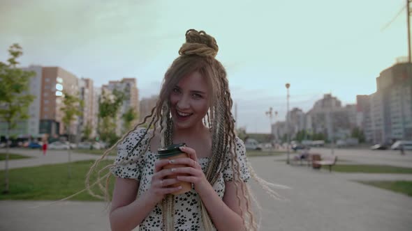Young Girl with Dreadlocks with Coffee Walks on the Street