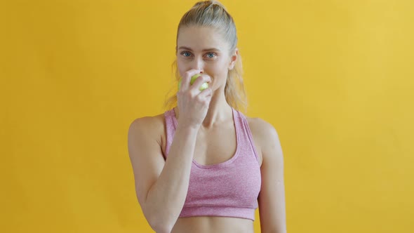Cute Sportswoman Eating Apple Enjoying Fresh Fruit on Yellow Background alt