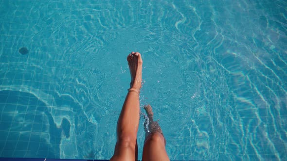Woman is Swinging Her Legs in Clear Water of Swimming Pool Happy Summer Vacation alt