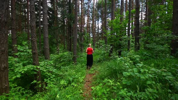 Woman in red top walking through woods in Poprad Slovakia. Dense forest with vibrant green foliage. alt