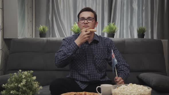 Young Man Eating Pizza and Watching Football While Sitting on Sofa in Apartment