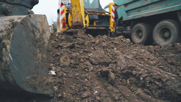 Excavator arm scoops up a bucket full of soil and rocks during roadworks in the countryside