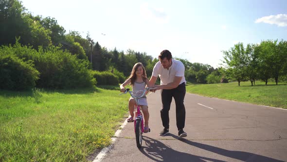 Young Father Teaching His Daughter to Ride Bicycle Outdoors alt