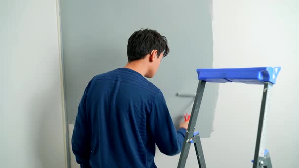 A Hearing-impaired Young Man in Hearing Aids Paints the Wall with a Roller Gray. alt