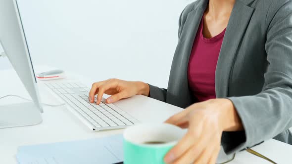 Businesswoman having coffee while working at desk alt