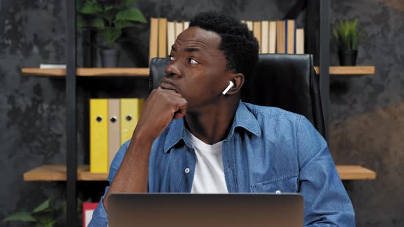 Thoughtful African American Man Sits on Chair at Table Works Laptop in Office alt