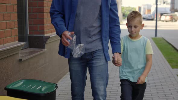 Close View of the Dad with Son Holding the Plastic Bottle and Put It Into the Special Garbage Bin alt