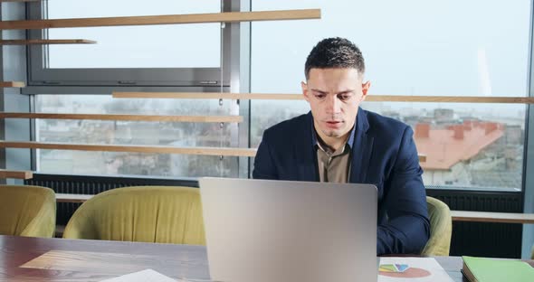 Concerned Man Working on Laptop Computer and Looking Away Thinking Solving Problem at Office alt