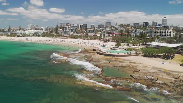 Aerial drone footage of ocean waves on a busy Kings beach, Caloundra, Australia