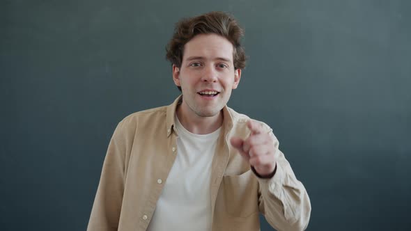 Slow Motion Portrait of Cheerful Person Pointing at Screen Smiling and Waving Hand alt