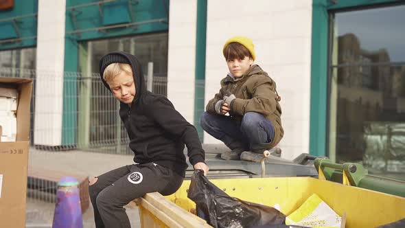 Lonely Street Children in Dirty Wear Spend Time Together Outdoors Sitting on Trash Cans alt