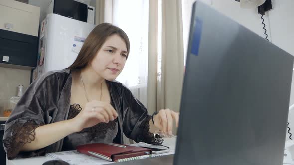 The Young Woman Works at Home at the Computer