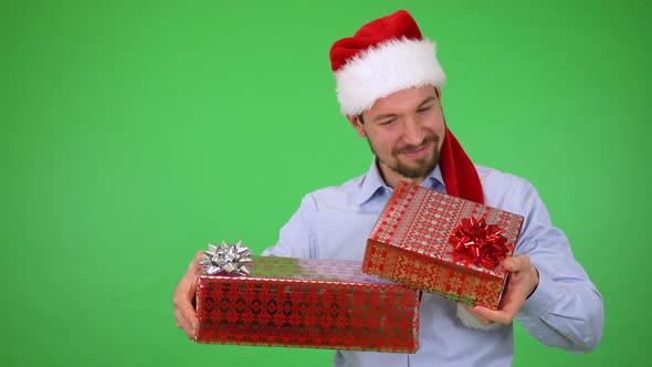 A Man in Christmas Hat Holds Presents and He Is Happy with Them and Smiles To Camera - Green Screen alt