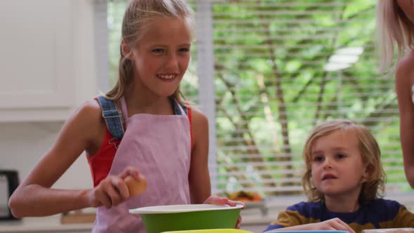 Happy caucasian mother in kitchen with daughter and son, wearing aprons, girl breaking egg into bowl alt