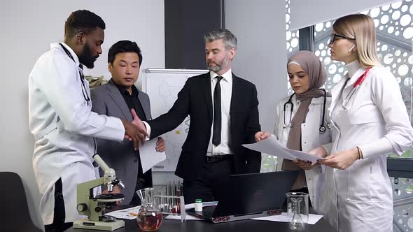 Multi Ethnic Team of Successful Doctors Finishing Clinical Trials on Computer with Handshake alt
