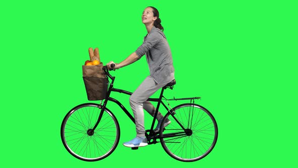 Casual woman riding a bicycle over a green screen, looking around and smiling. 4K alt