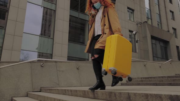 European Woman Going with Yellow Suitcase and Talks on the Phone in Protective Face Mask alt