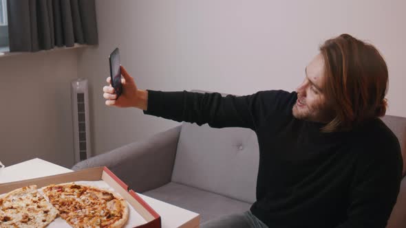 Young Caucasian Man Having a Video Call and Showing Pizza To His Family alt