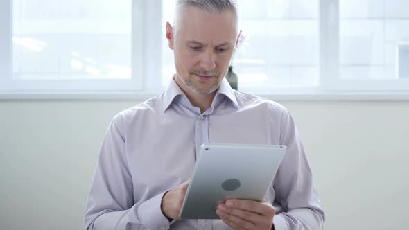 Middle Aged Man Browsing Internet on Tablet in Office alt