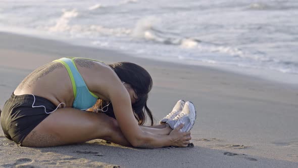 Woman Sitting on Beach and Stretching alt