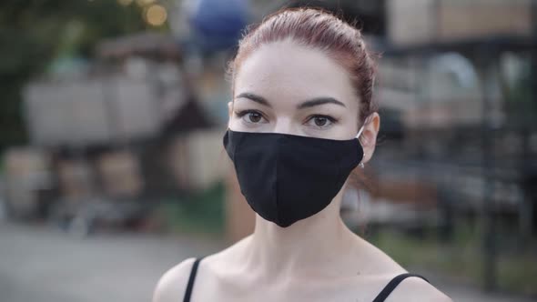 Closeup Portrait of Young Slim Caucasian Redhead Woman in Black Covid Face Mask Looking at Camera alt