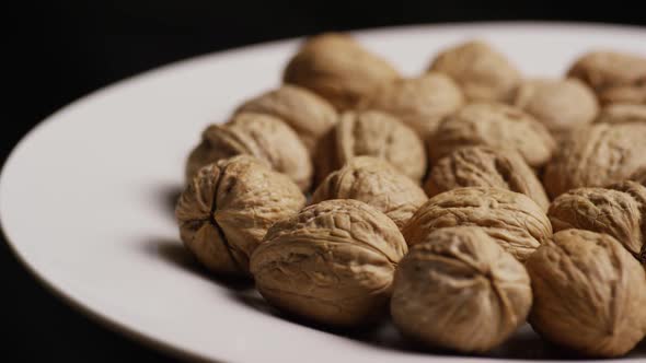Cinematic, rotating shot of walnuts in their shells on a white surface - WALNUTS  alt