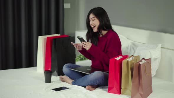 happy woman using smartphone for online shopping with credit card on a bed