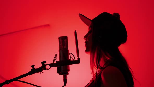 Silhouette of Profile Woman Singer in Cap and Headphones Artist Sings Song in Recording Studio