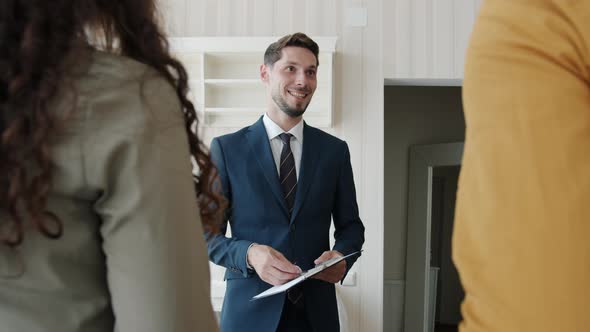 Joyful Real Estate Broker Giving Keys to Happy Customers Shaking Hands Indoors in New House alt