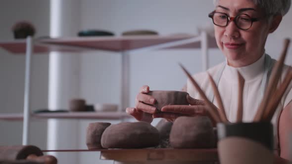 Asian elderly woman enjoying pottery work at home. alt