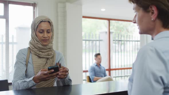 Smiling biracial woman paying with credit card at reception at modern dental clinic alt