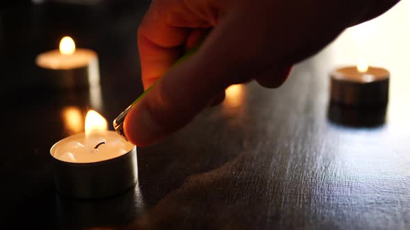 Lighting a single small tealight candle flame in slow motion with other fires burning and dancing in alt