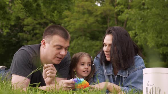 Happy Family Relaxing in Nature and Playing with a Toy Pop It alt