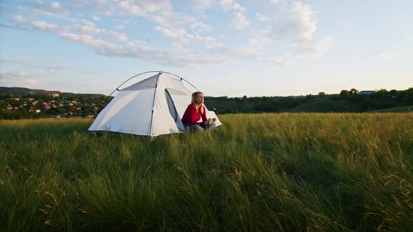 a Young Woman Happily Set Up a Tent on the Mountain Hills During Sunset for Rest After a Hike alt