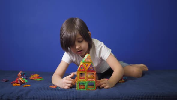 Boy Child in a White Tshirt is Sitting on a Bed Against a Blue Wall and Playing alt