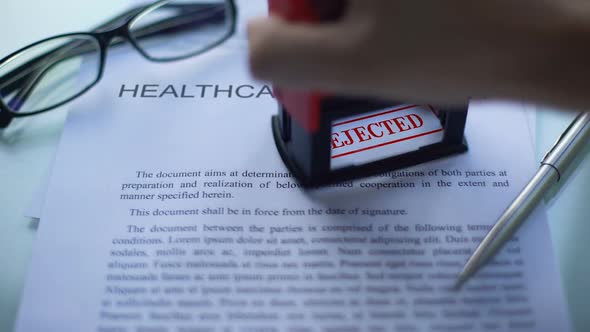 Healthcare Contract Rejected, Officials Hand Stamping Seal on Business Document alt