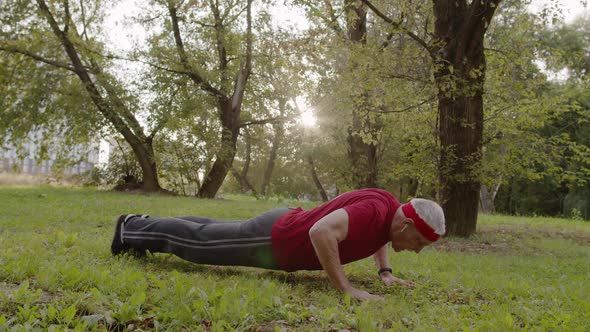 Elderly Sporty Man Doing Push Up Exercises. Workout Cardio Outside in City Park at Morning alt
