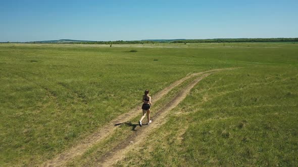 Slim Sportswoman Running on Path in Meadow. Pan Around Drone View of Fit Female Athlete Running