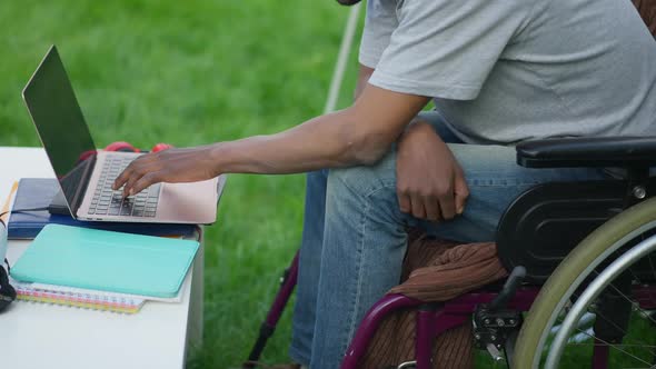 Unrecognizable African American Adult Man in Wheelchair Typing on Laptop Keyboard in Slow Motion alt