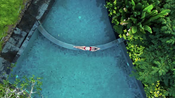 Young Woman in Red Bikini Lays on Blue Water Pool alt