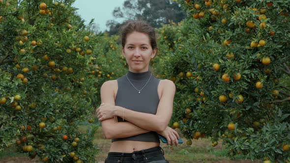Girl Standing and Smiling in an Orange Orchard Looking Straight at the Camera alt
