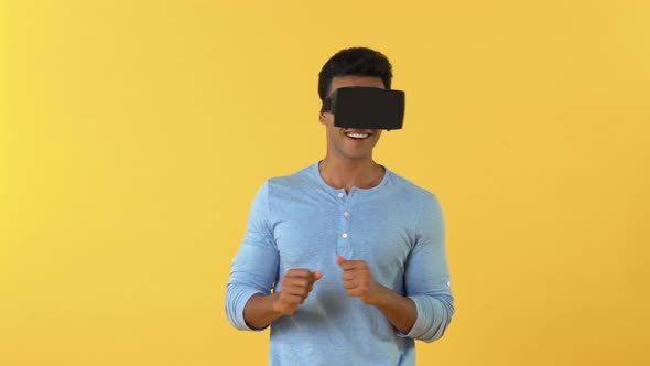 Happy Indian man enjoying with VR gadget isolated on yellow background
