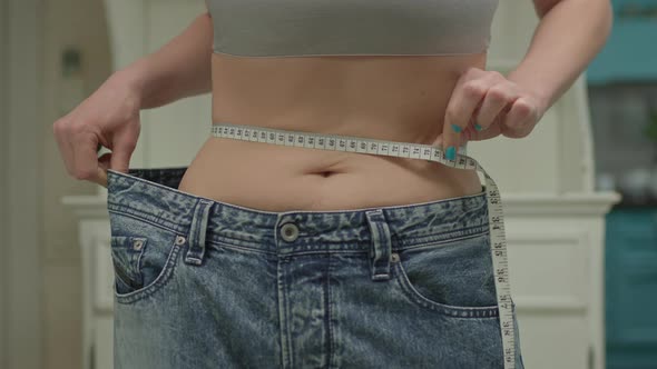 Close Up of Woman Measuring Her Waistline Wearing Oversized Jeans After Weight Loss alt