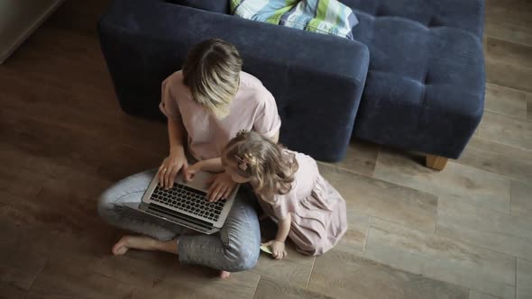 Mother Is Teaching Her Little Son To Work on Laptop Sitting on Floor at Home