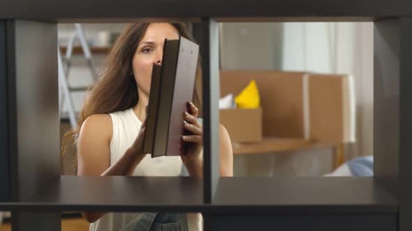 Happy Young Woman Putting Books on Shelf Unpacking at New Apartment alt