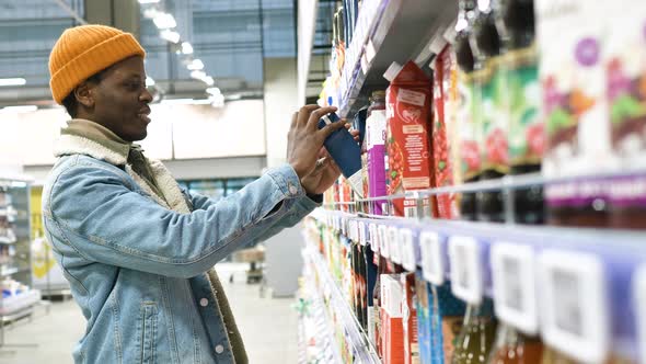 African American Guy in Hat and Jacket Chooses Juice in Shop alt